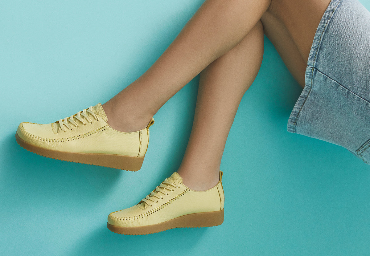 Yellow sneakers worn with light blue denim skirt on a teal background